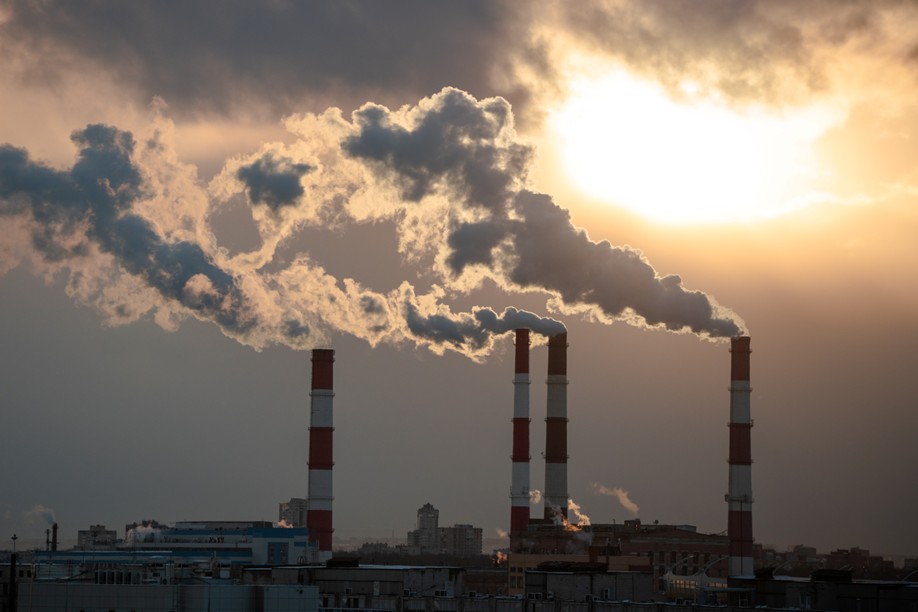 Industrial smokestacks billowing smoke with cityscape in background