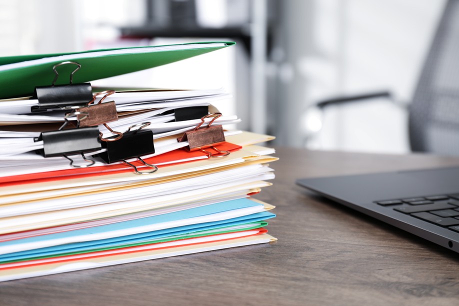 Stack of bundled papers and file folders with open laptop in the background