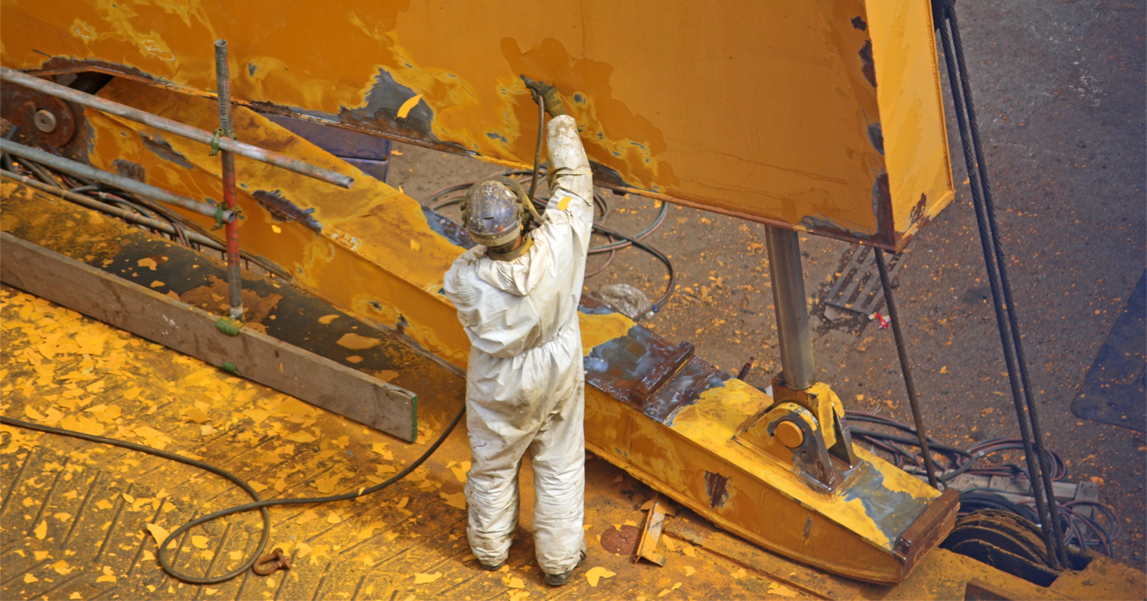 Shipyard worker stripping paint from machinery