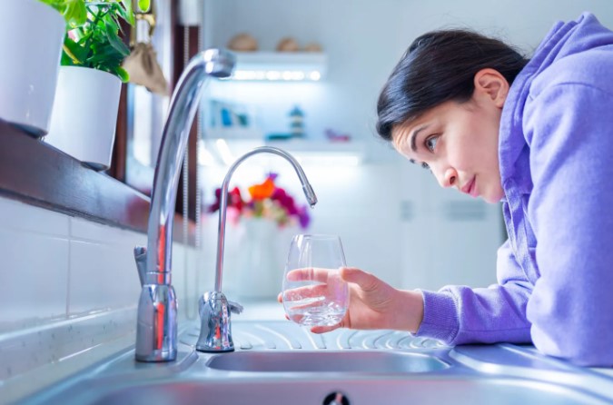Person filling up glass with tap water from faucet